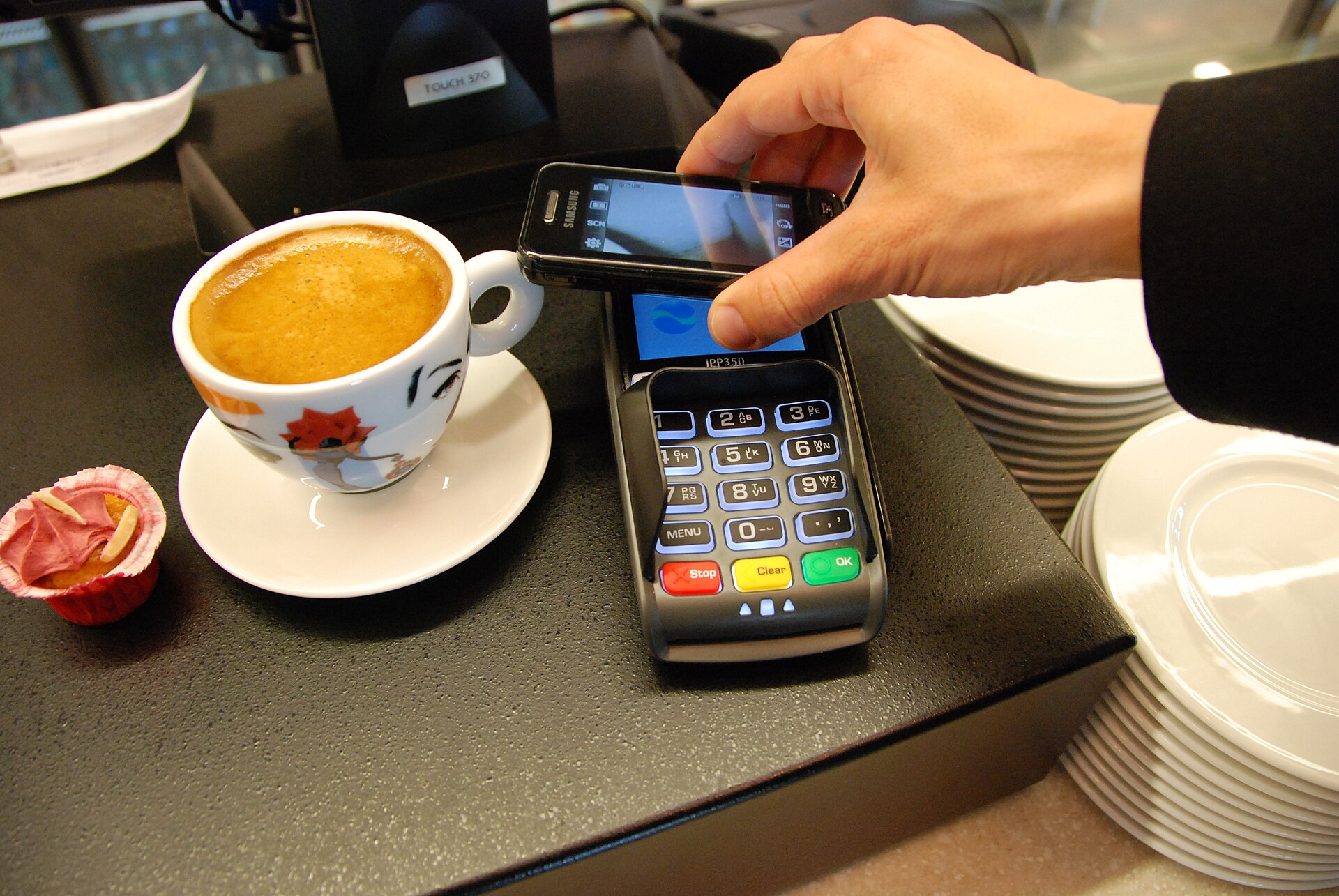 カフェの決済端末にスマートフォンをかざして支払う様子