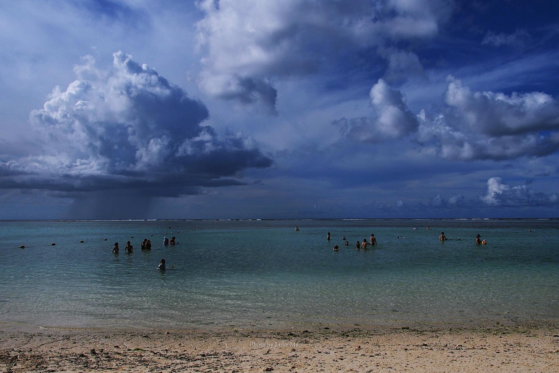 グアム・タモン湾のビーチと沖に降る雨雲